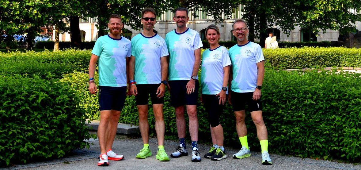 Fünf Personen in sportlichen T-Shirts stehen vor grüner Vegetation.