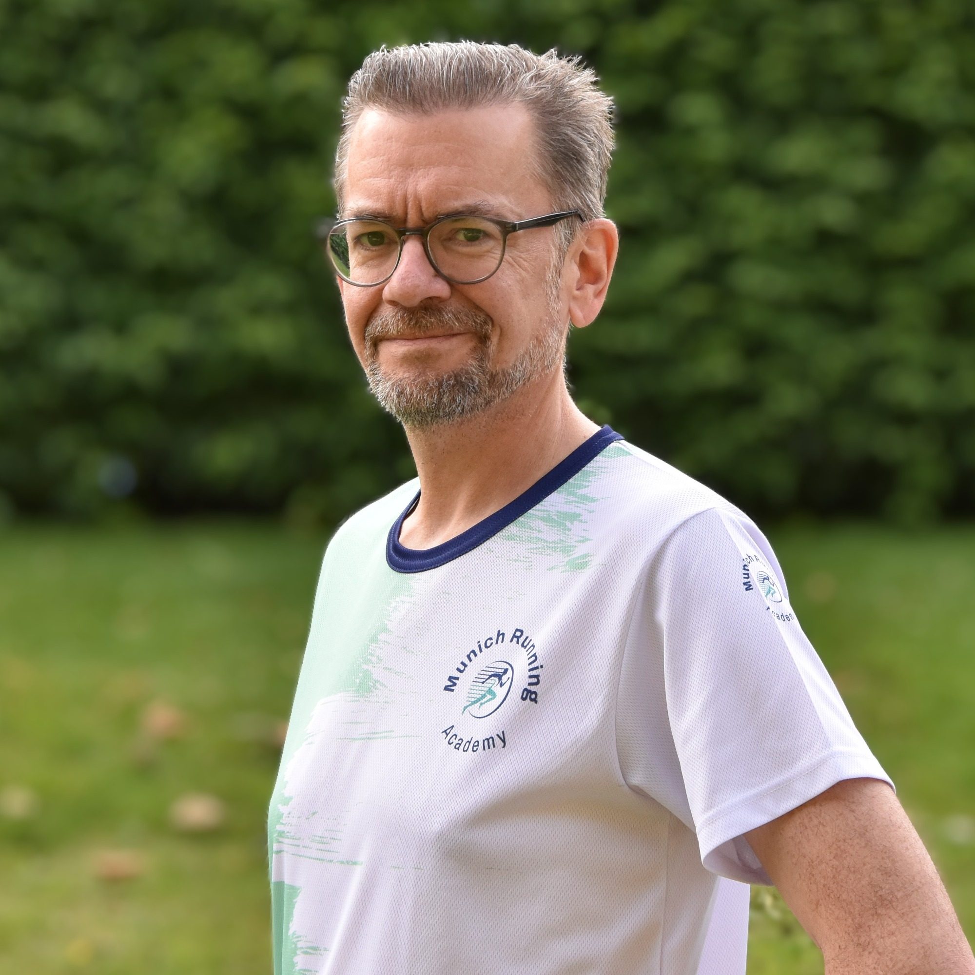 Mann mit Brille und Kurzhaarschnitt trägt ein weißes T-Shirt, steht im Freien.