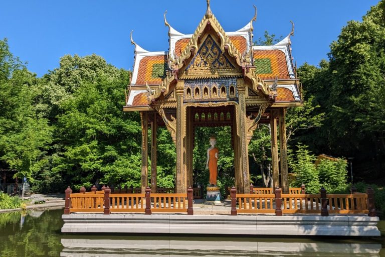 Thailändischer Pavillon umgeben von grüner Landschaft und einem klaren Himmel.