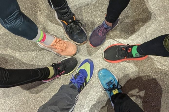 Sechs verschiedene Sportschuhe stehen in einem Kreis auf einem grauen Boden.